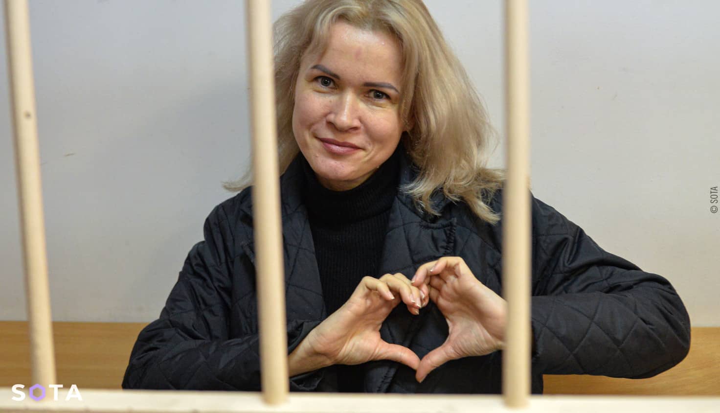 Maria Ponomarenko tras unas rejas haciendo un corazón con las manos